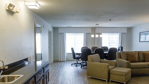 A spacious living room with a kitchen area, including a dining table with chairs, a sofa, and a large window providing natural light. - Holiday Inn Bloomington-Airport by IHG (Bloomington)