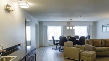 A spacious living room with a kitchen area, including a dining table with chairs, a sofa, and a large window providing natural light.