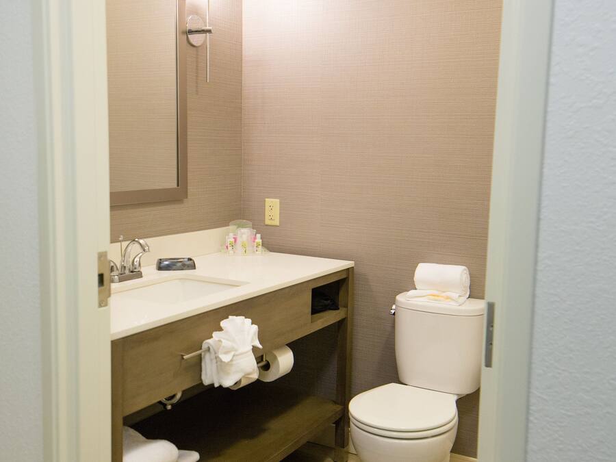 A bathroom with a wooden vanity, a sink, a mirror, a toilet, and a towel rack.