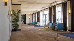 A hotel corridor with seating areas, a large potted plant, and a patterned carpet. - Holiday Inn Bloomington-Airport by IHG (Bloomington)