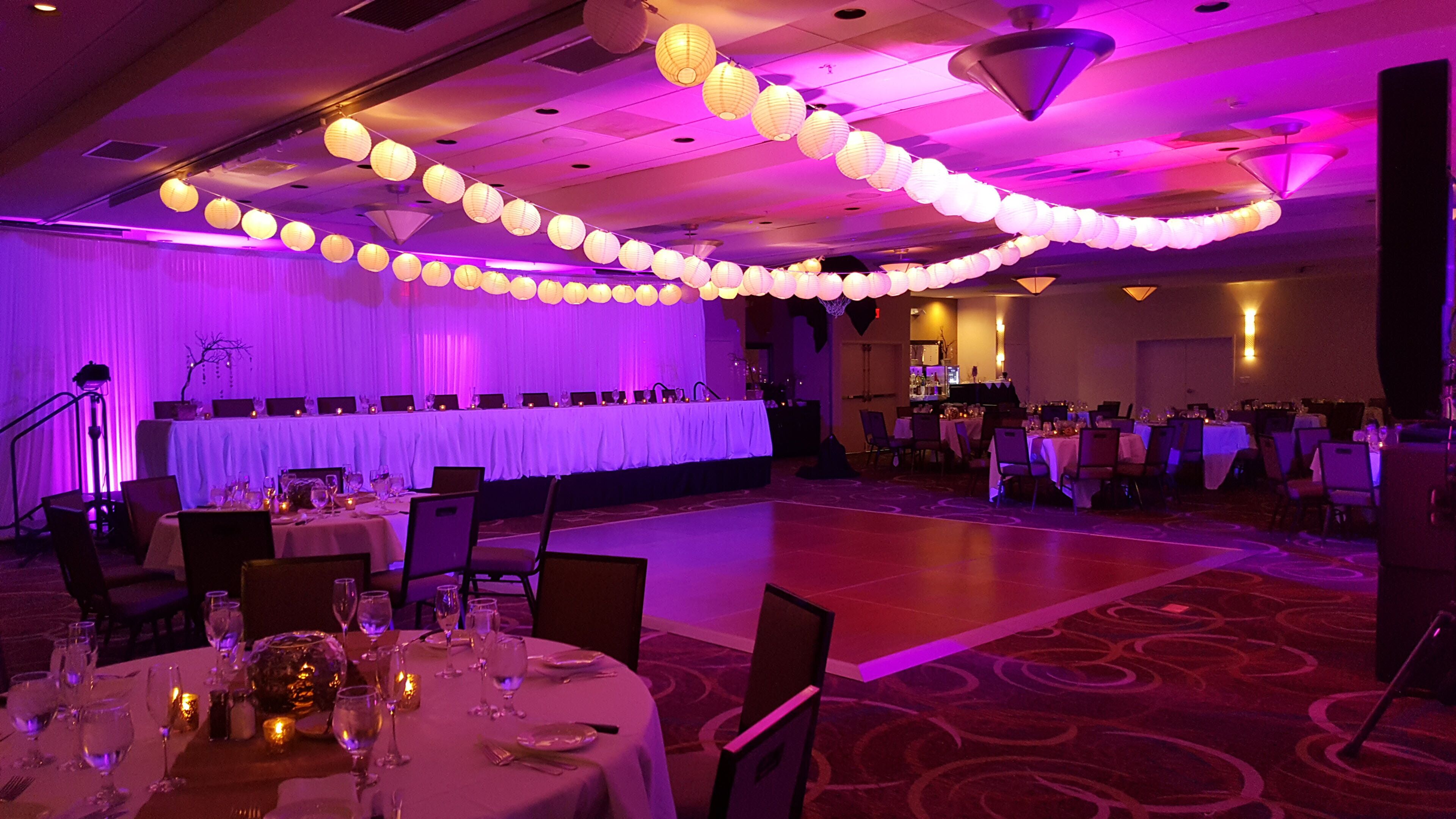 A banquet hall with round tables set for dining, a stage with draped curtains, and a dance floor.