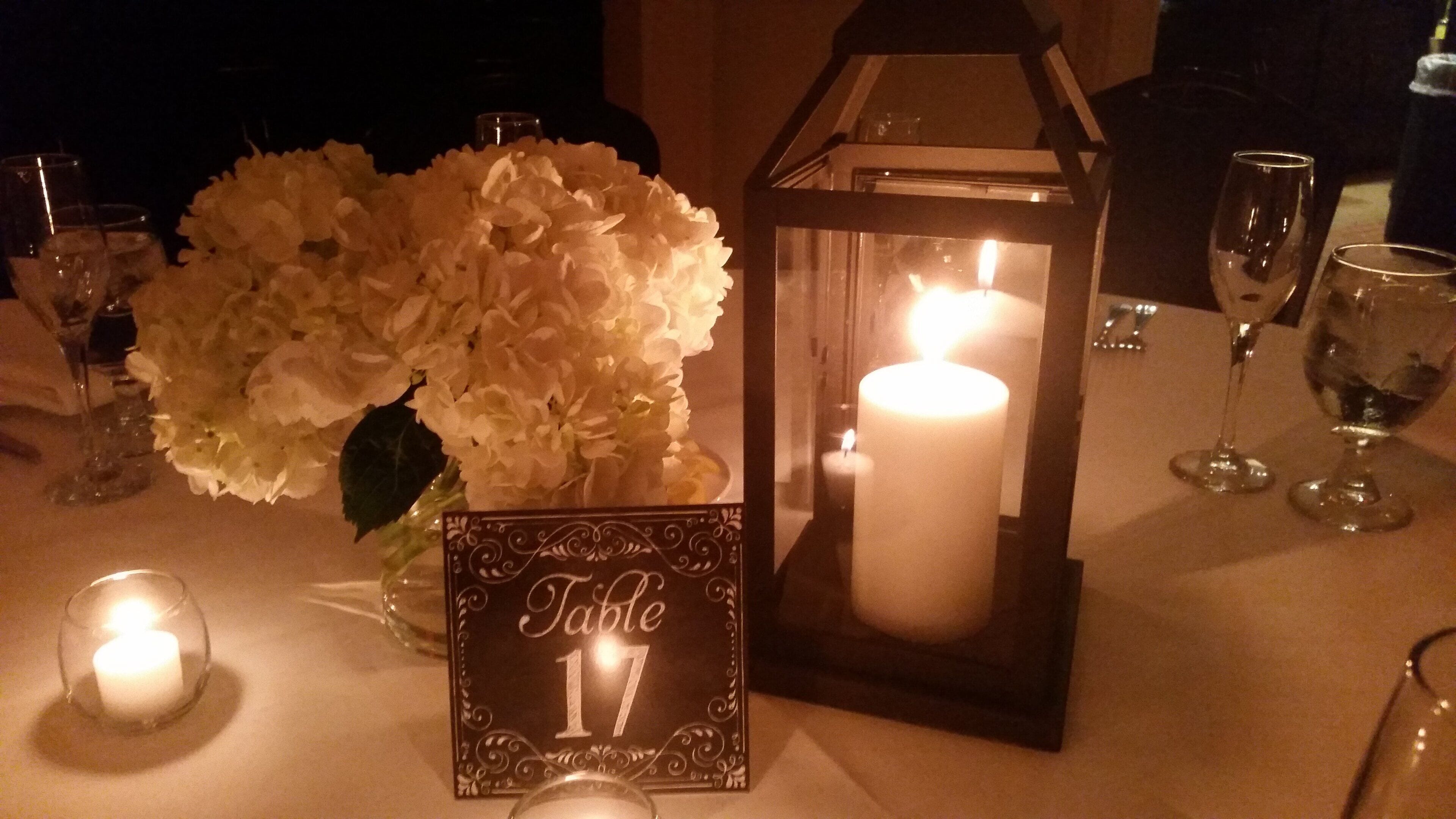 Una mesa dispuesta con una vela encendida, un centro de mesa floral y un cartel con el número de la mesa.
