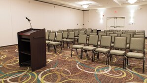 A conference room with rows of chairs, a podium, and an exit sign. - Holiday Inn Bloomington-Airport by IHG (Bloomington)
