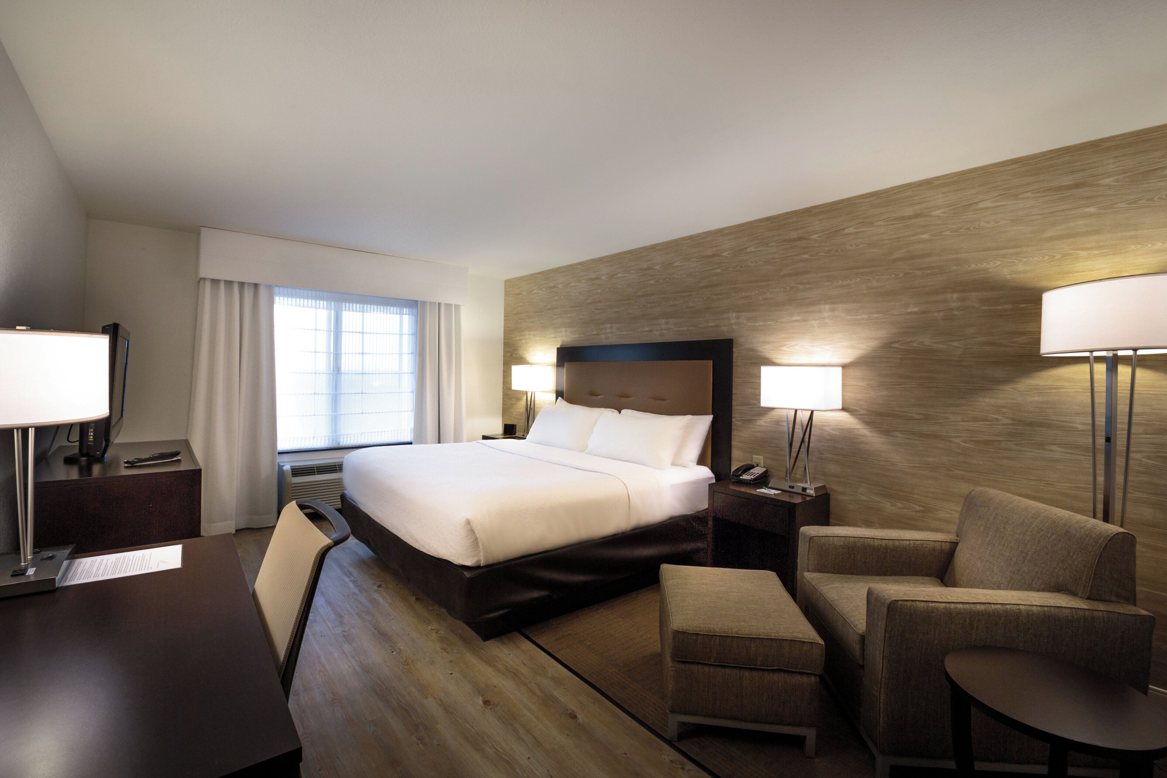 Une chambre d’hôtel avec un lit, un bureau, une chaise, un canapé et une lampe.