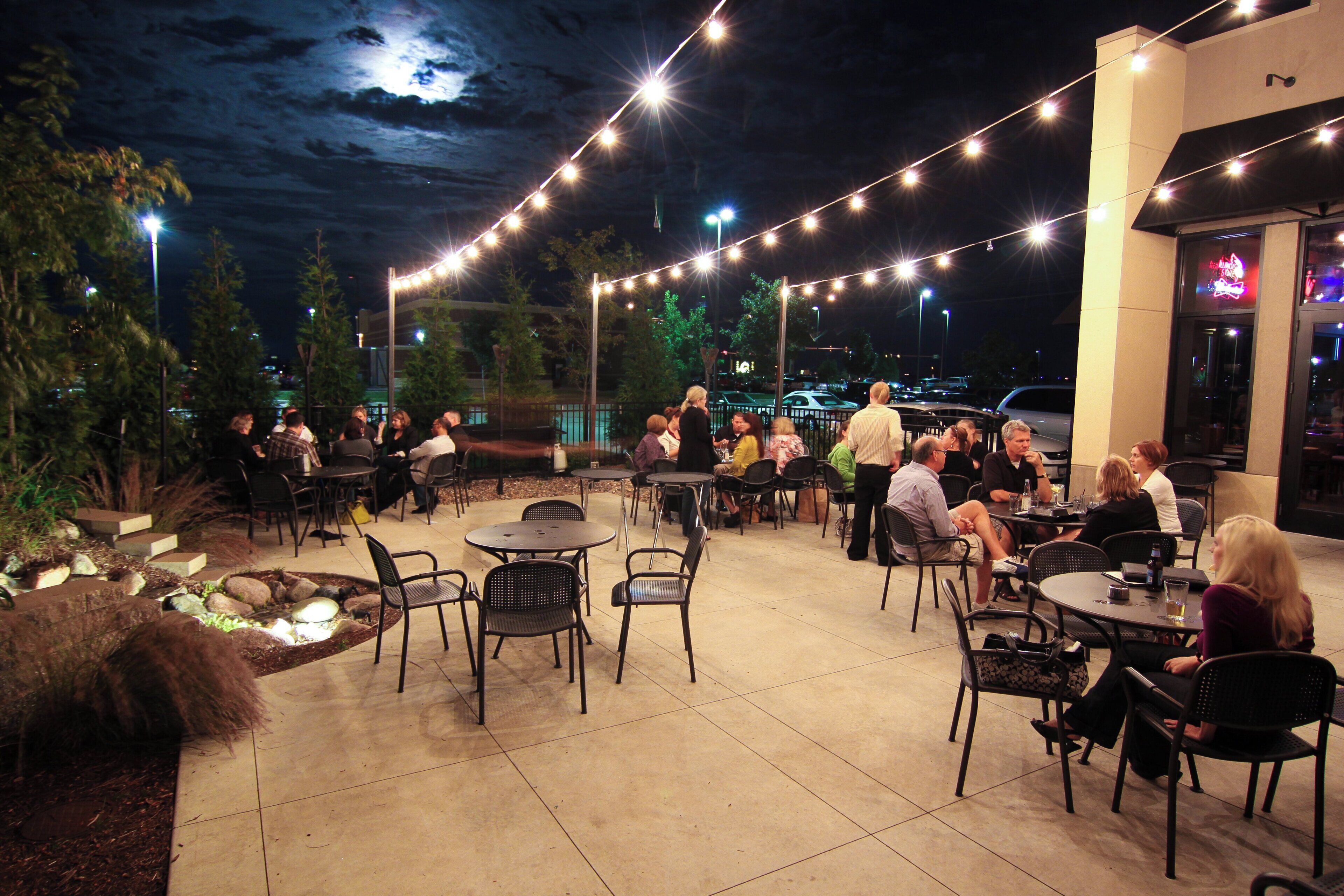 An outdoor patio area with tables and chairs, string lights, and a small water feature.