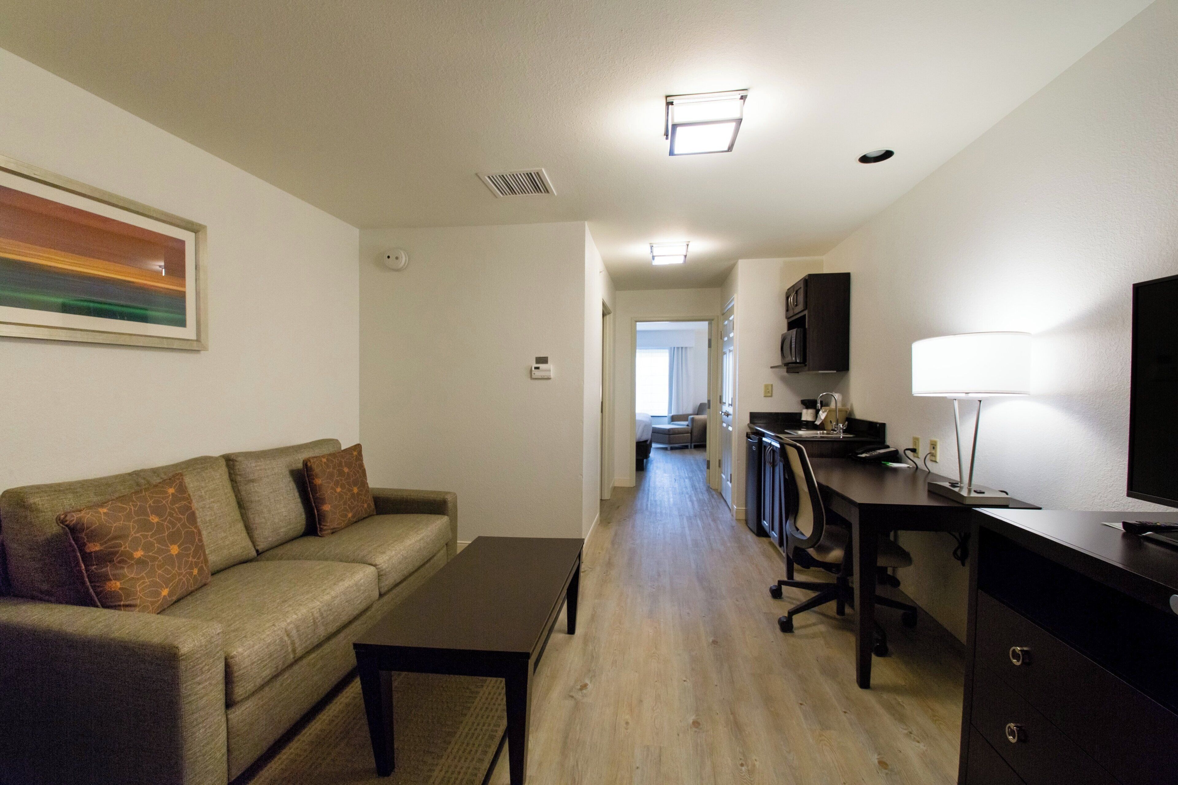 A hotel room with a sofa, a desk, a television, and a kitchenette.