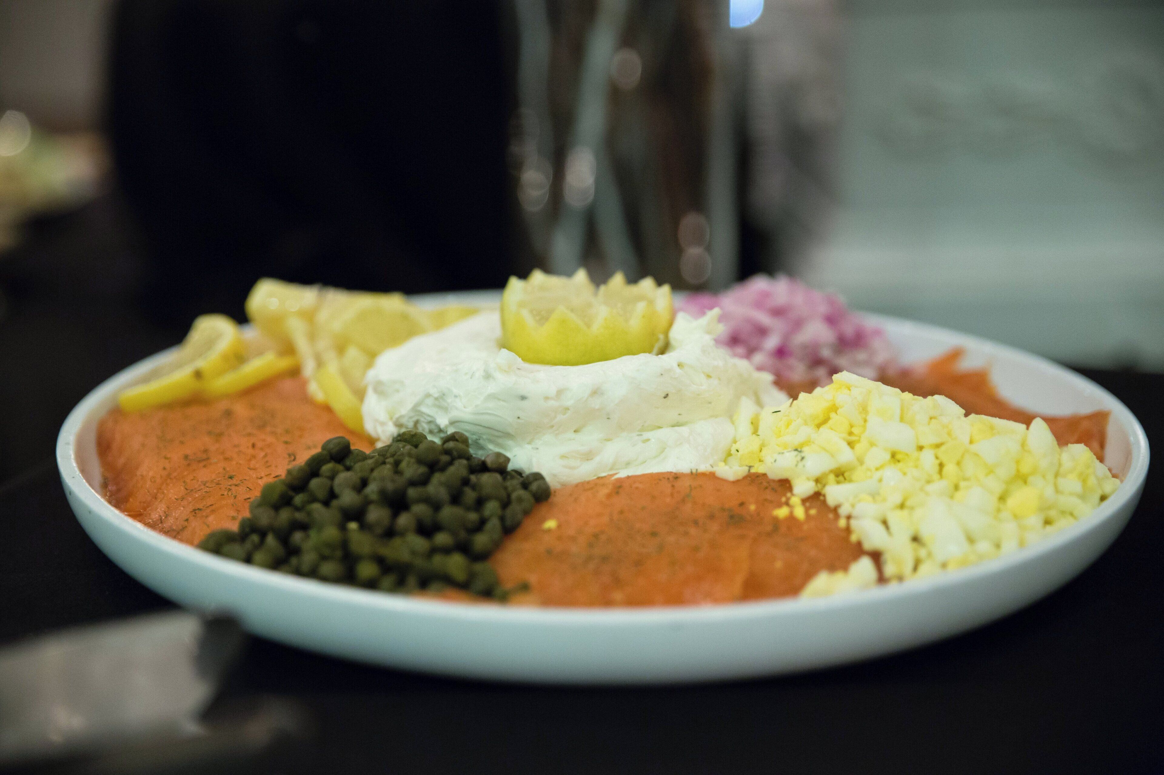 Un plato con diferentes alimentos, incluyendo una cucharada de crema, verduras picadas y una porción de carne.