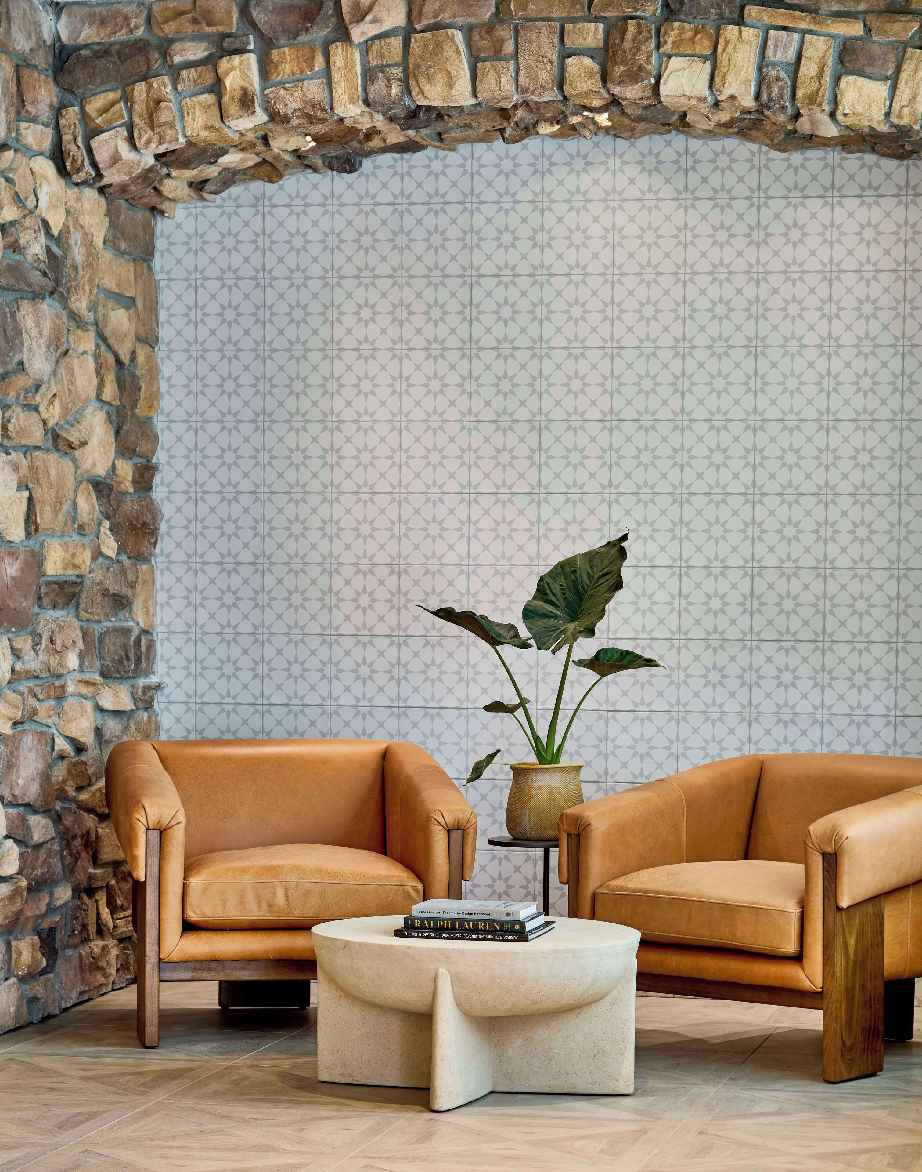 A cozy seating area with two leather armchairs and a round coffee table, set against a patterned wall and a stone archway.