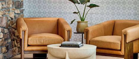 A cozy seating area with two leather armchairs and a round coffee table, set against a patterned wall and a stone archway.