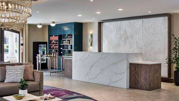 A modern hotel lobby with a reception desk, seating area, and a bar.