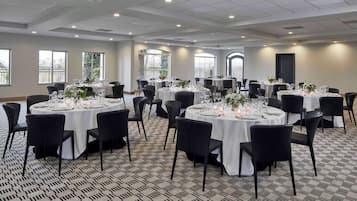 A large conference room with multiple round tables set for dining, featuring black chairs and white tablecloths.