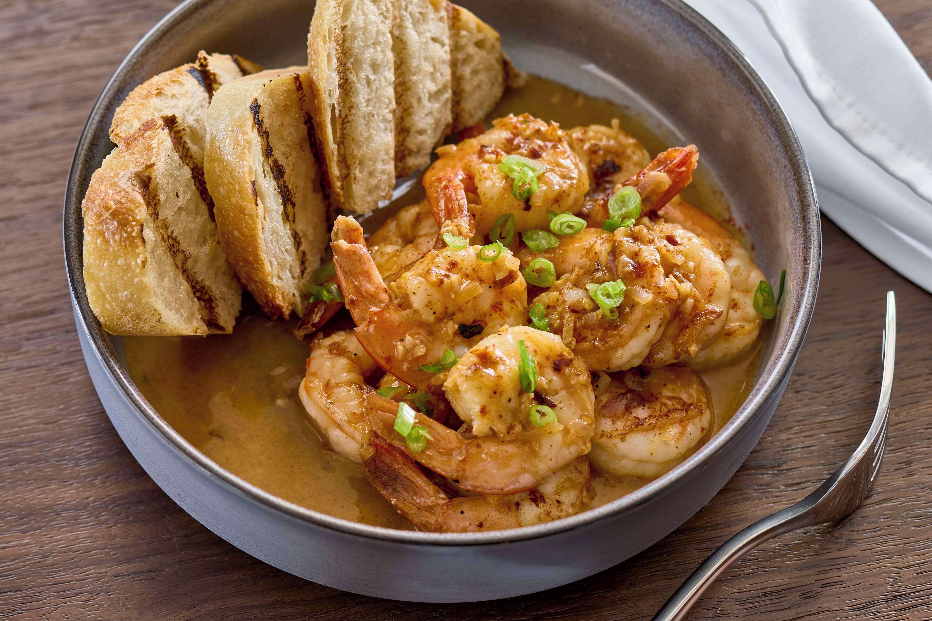 Un bol de crevettes accompagné de pain sur une table en bois.