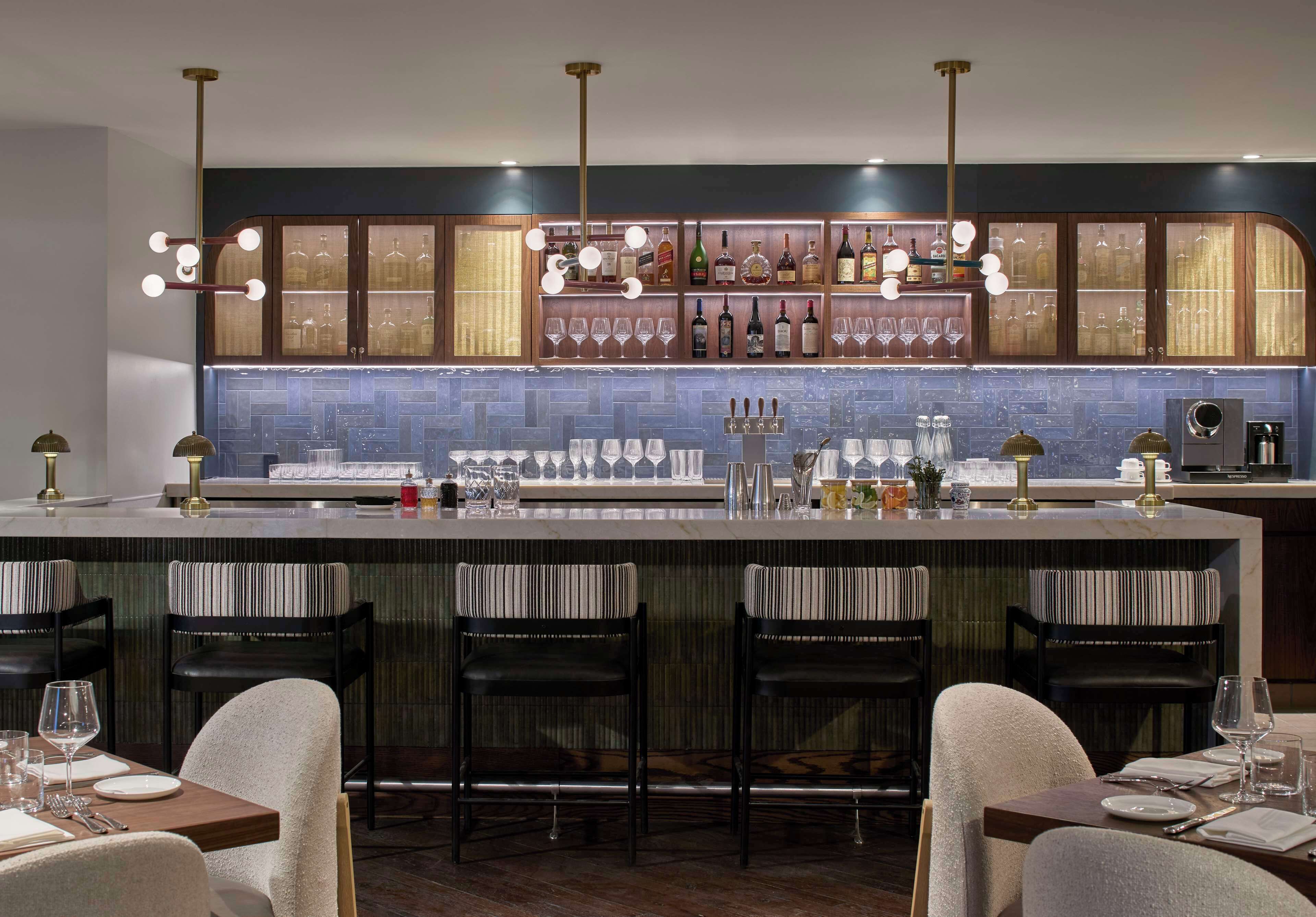 A modern bar area with a bar counter, stools, and a variety of bottles and glasses.
