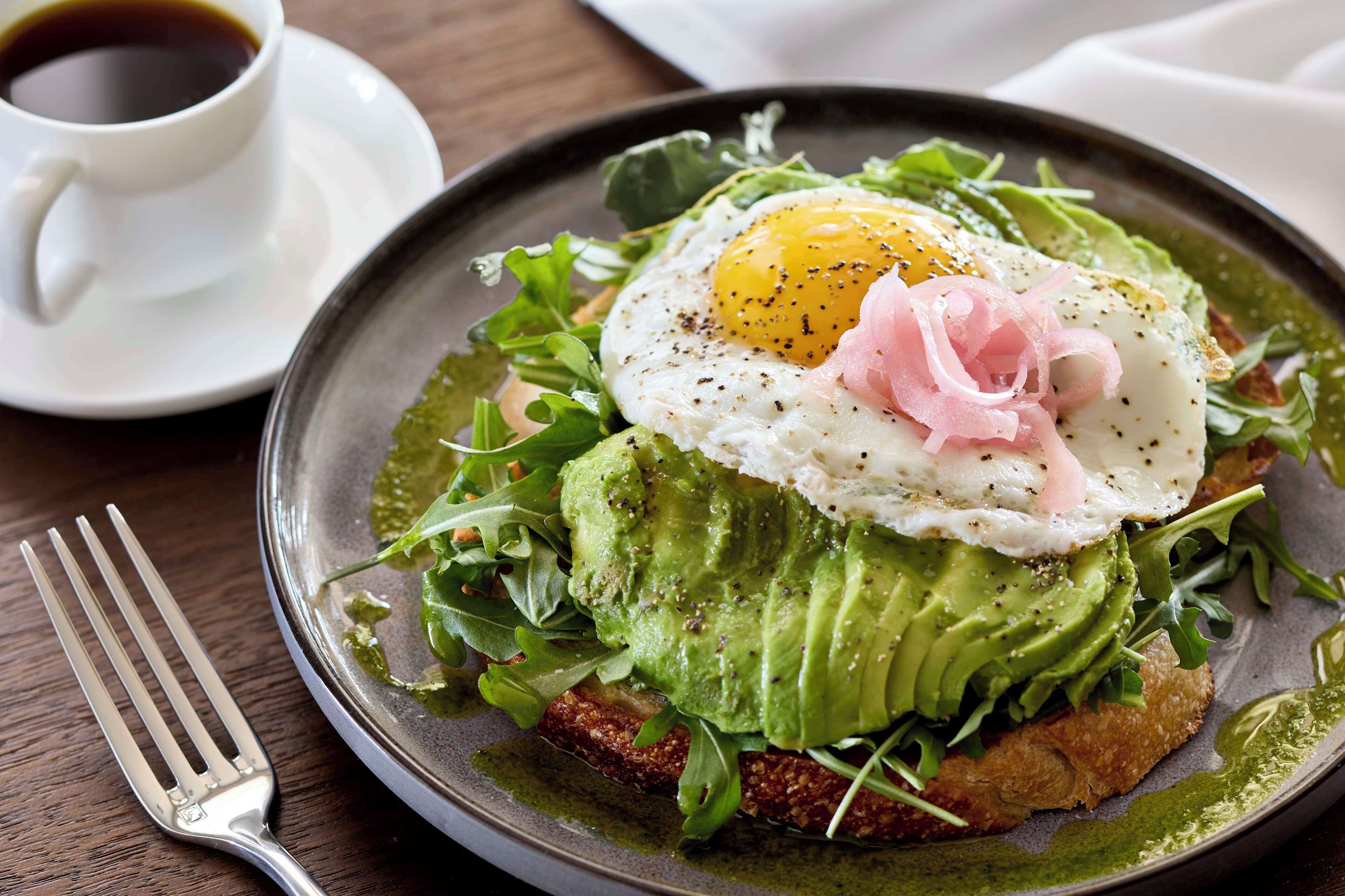 A plate with a poached egg, avocado, and greens, accompanied by a cup of coffee.