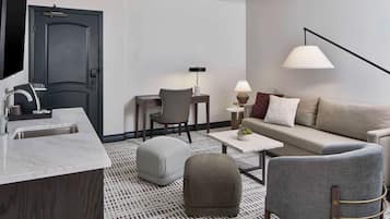 A modern hotel room with a marble kitchen island, a grey sofa with a patterned rug, and a minimalist decor style.