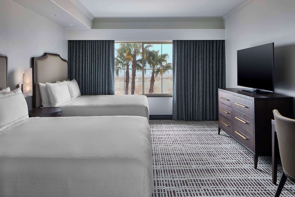 A hotel room with two beds, a TV, a dresser, and a view of palm trees.