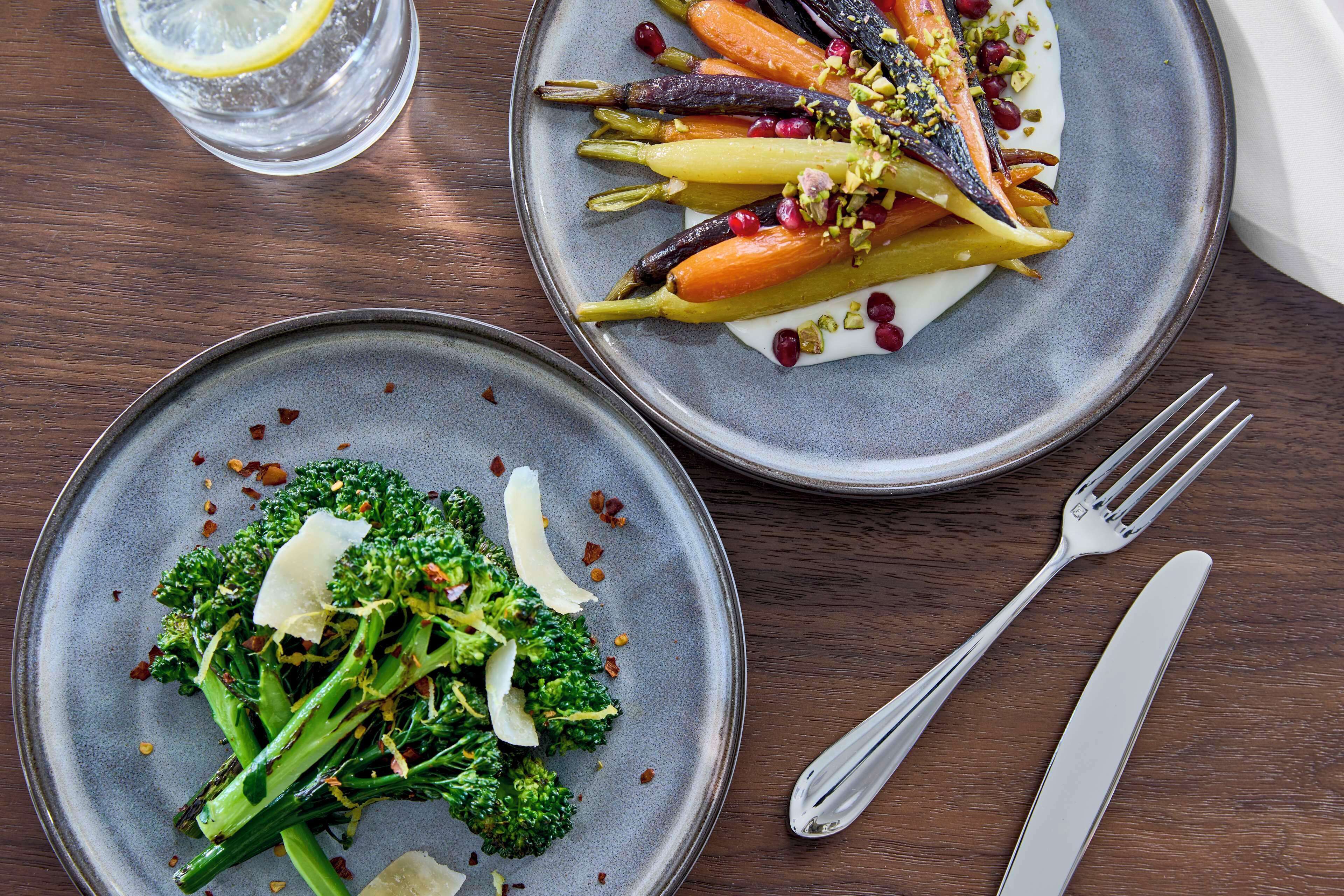 Two plates of food on a wooden table with a fork and knife beside them.