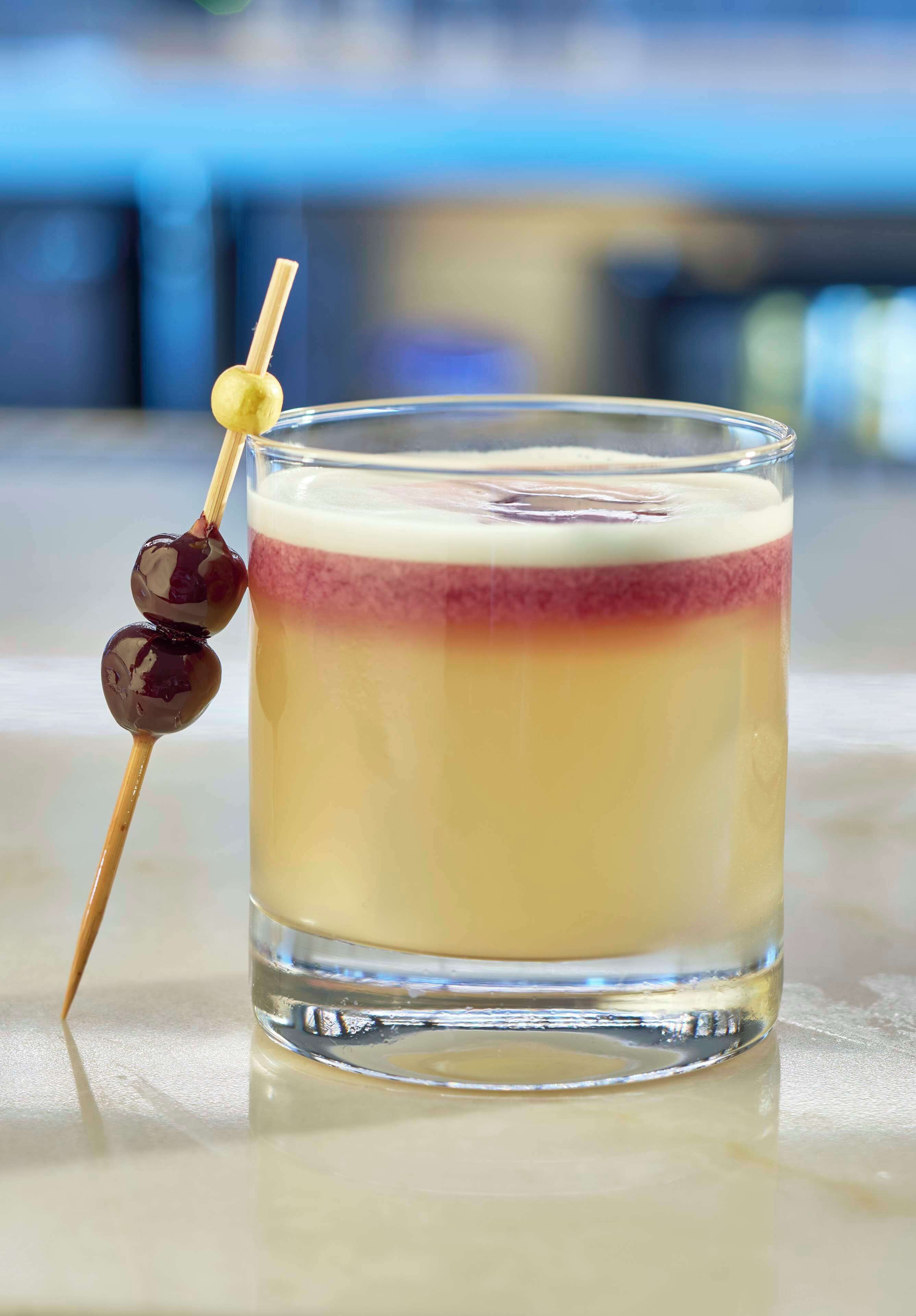 Una bebida en capas con un brochete de cerezas al lado.