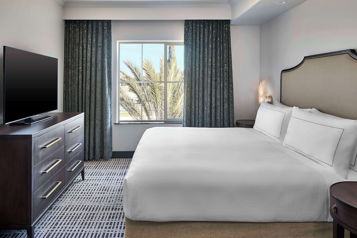 A hotel room with a large bed, a dresser, a television, and a window with curtains.