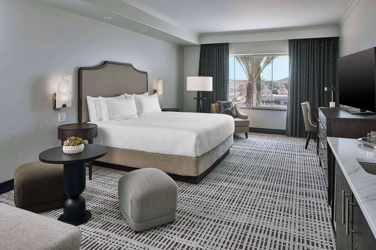 A hotel room with a large bed, a desk, a chair, a TV, and a window with curtains.