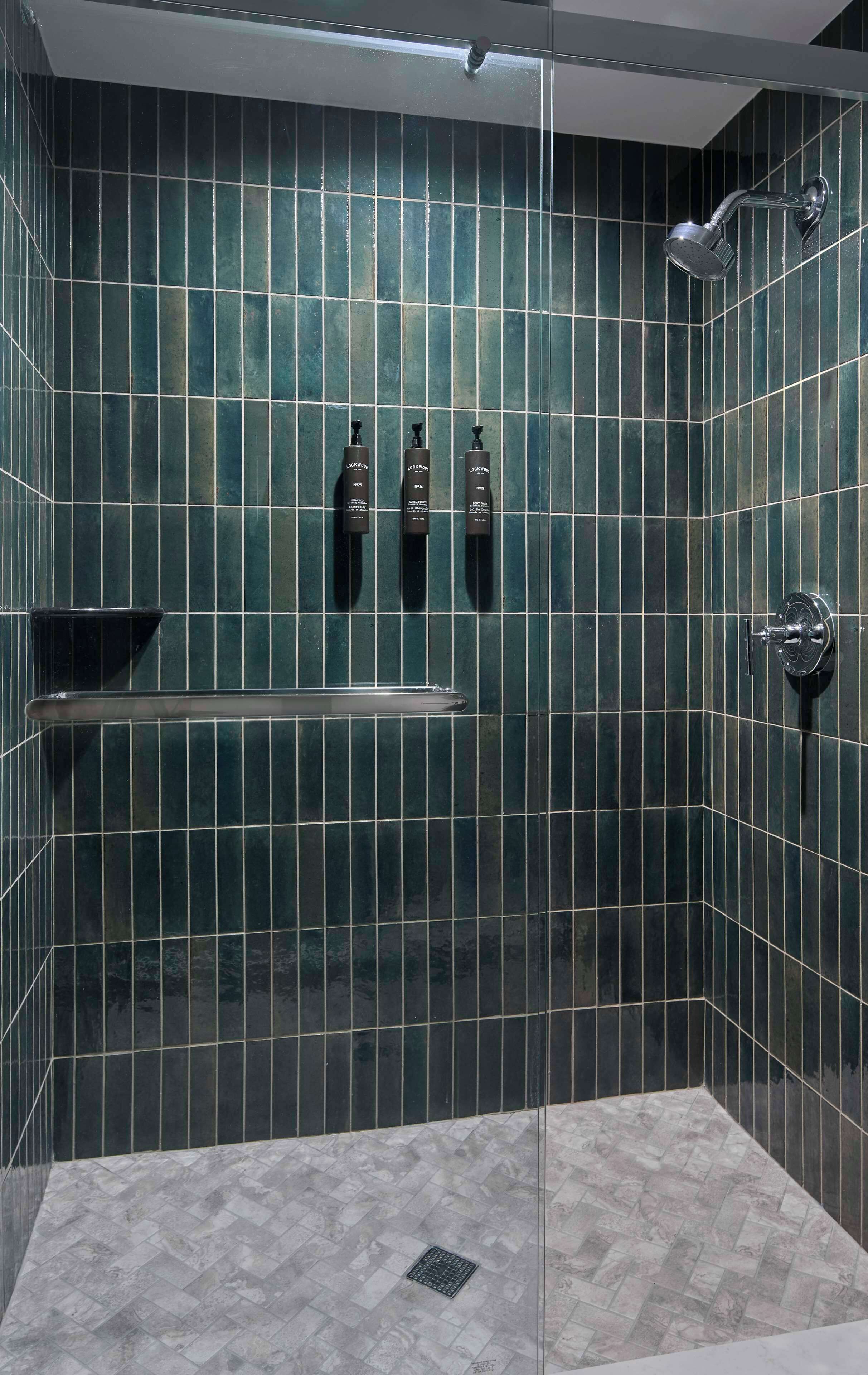 Un espace douche moderne avec des carreaux vert foncé, une douche à l’italienne en verre et un sol en marbre.