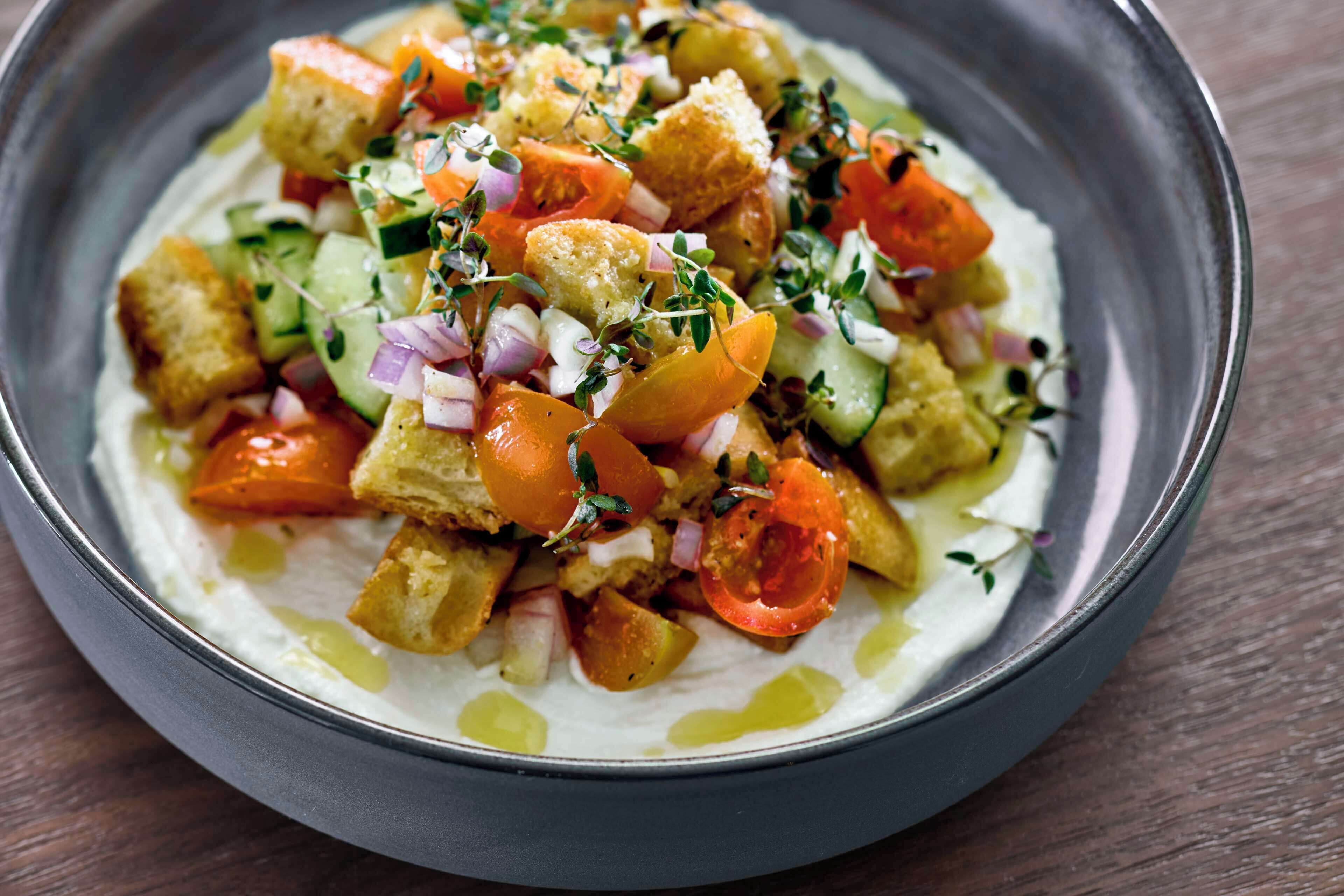 A bowl of salad with croutons, tomatoes, cucumbers, and onions, garnished with herbs.