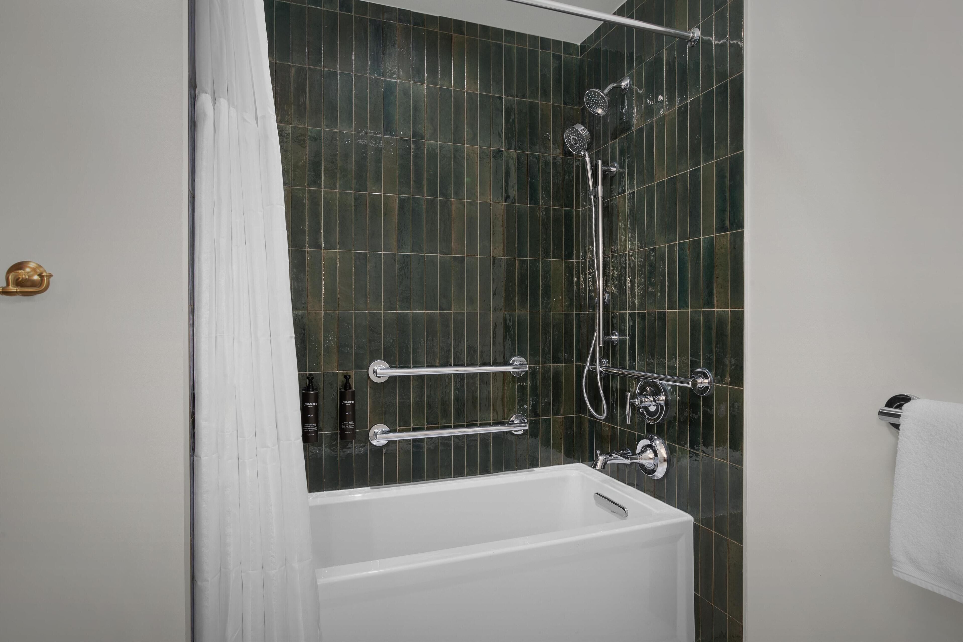 A modern bathroom with a bathtub, shower, and handrails.