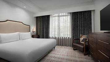 Une chambre d’hôtel avec un grand lit, une chaise en bois, une commode et une grande fenêtre avec des rideaux.