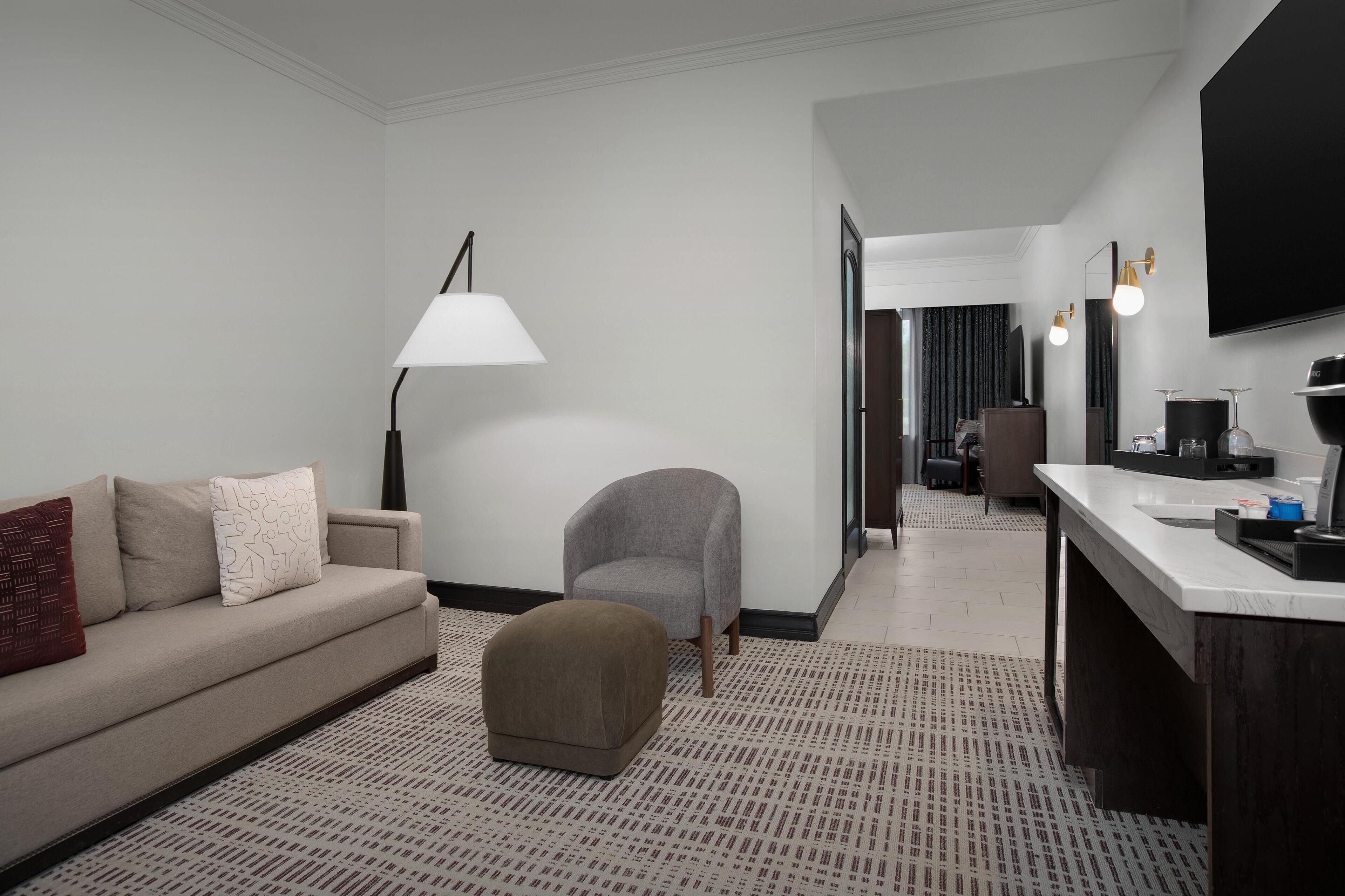 Habitación de hotel con sofá, reposapiés, lámpara y una zona de kitchenette.
