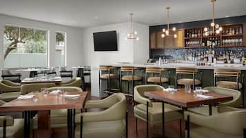 A restaurant with high tables and chairs, a bar area with shelves of bottles, and a large window with a tree view.