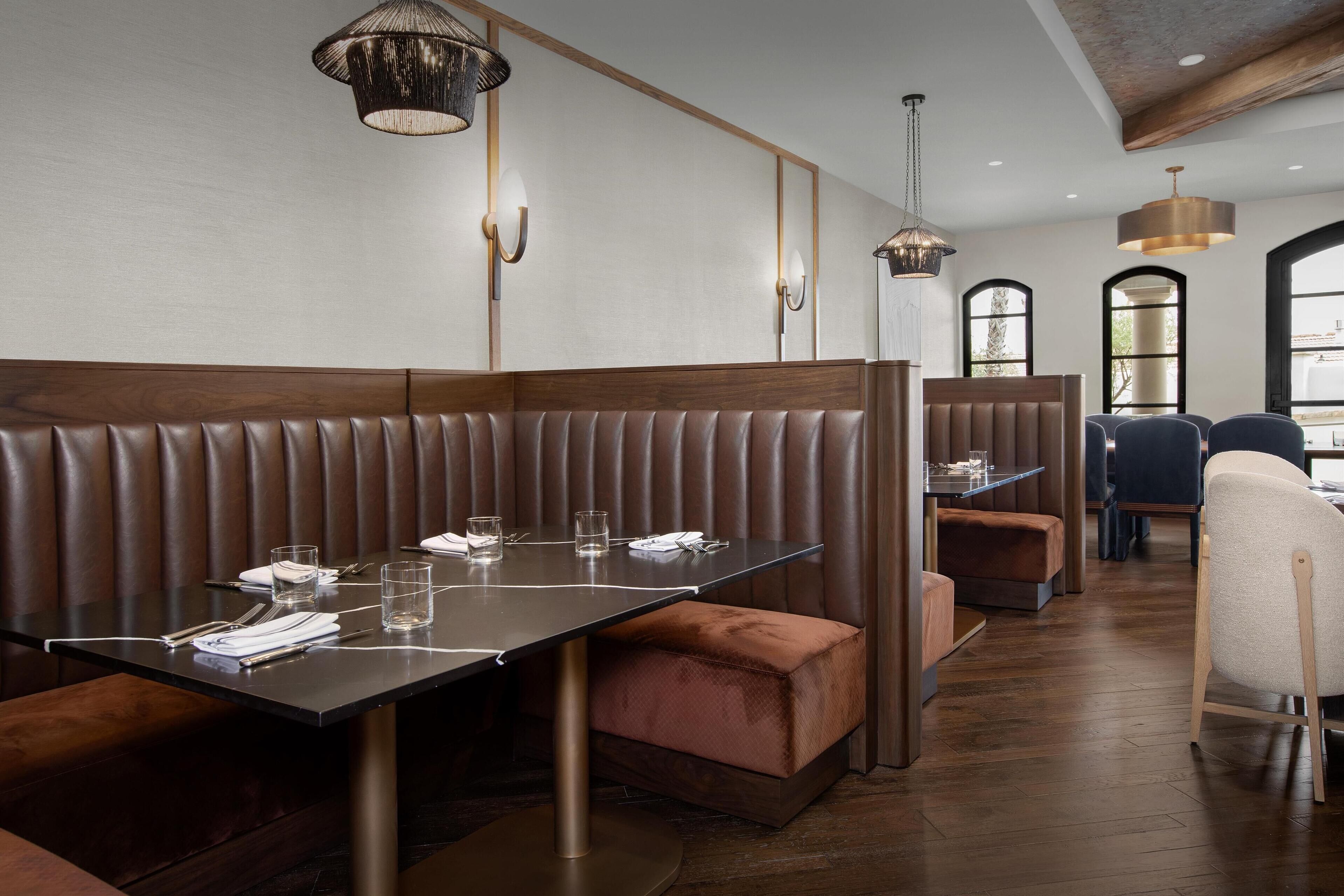 A restaurant with booth seating, pendant lighting, and a view of the city through large windows.