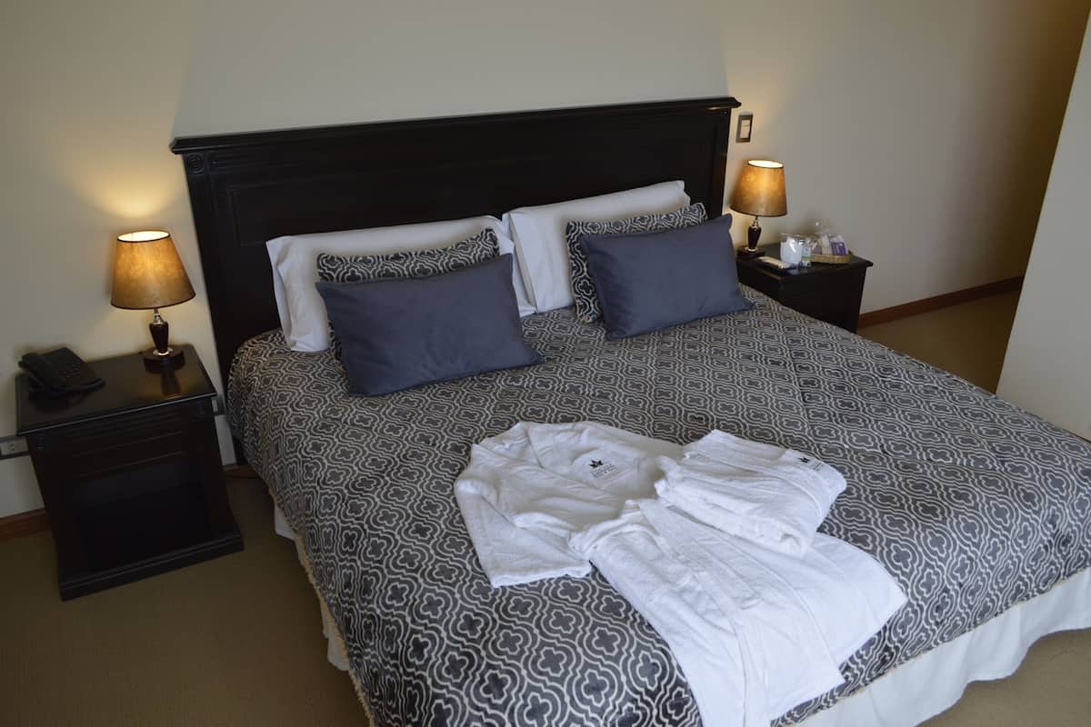 A hotel room with a large bed, two bedside tables, a lamp on each table, and a telephone on one of the tables.