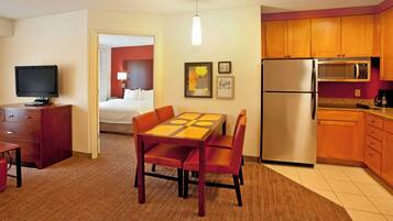 A hotel room with a dining table, chairs, a TV, a bed, a kitchen area with a refrigerator and microwave, and a carpeted floor.
