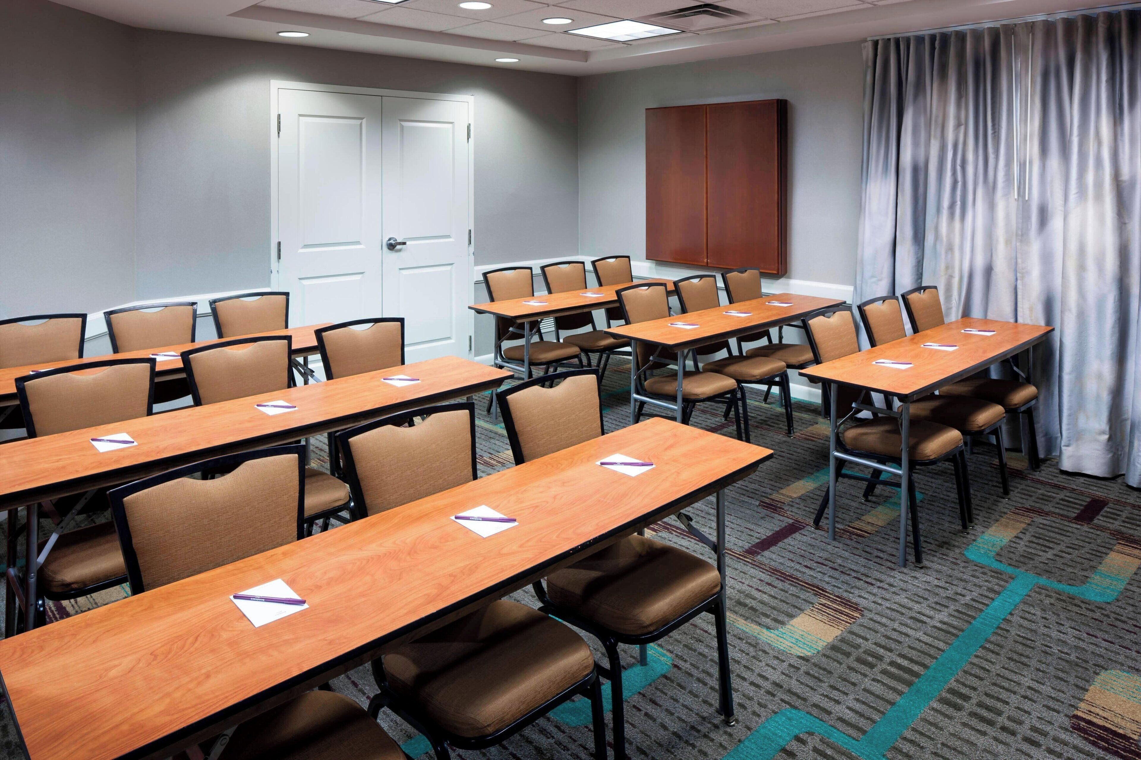 A conference room with multiple tables and chairs, a door, and a curtain.