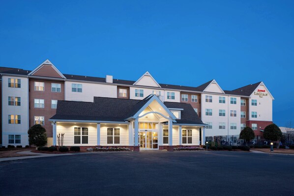 A multi-story hotel with a central entrance, multiple windows, and a parking lot.