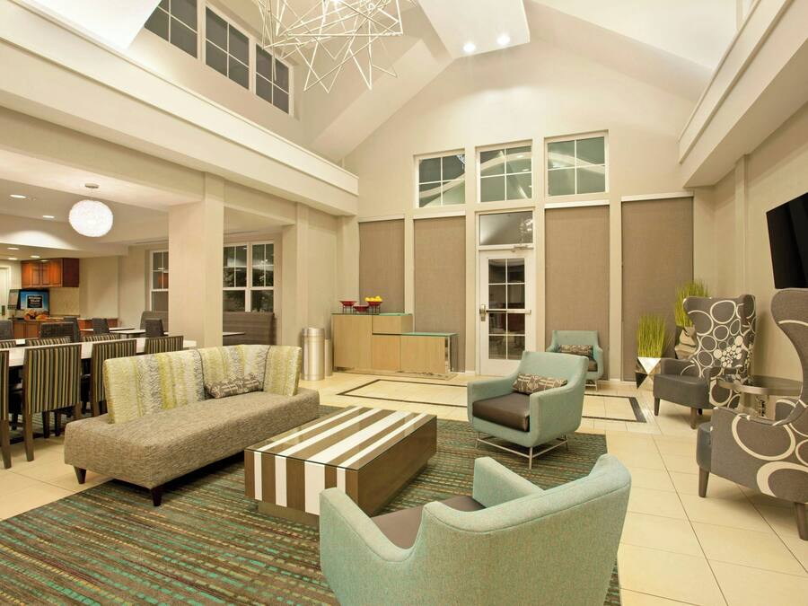 A spacious living area with a sofa, armchairs, and a coffee table. There is a dining area with chairs and a table, and a kitchen in the background.