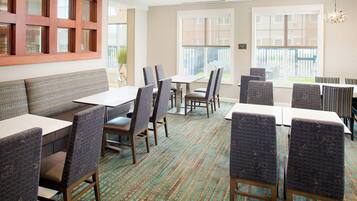 A hotel dining area with booths and tables, patterned chairs, and large windows offering a view.