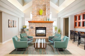 A spacious living room with a stone fireplace, teal armchairs, and a striped coffee table.