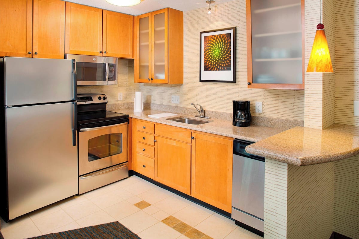 Una cocina moderna con armarios de madera, electrodomésticos de acero inoxidable, encimera de granito y una lámpara colgante decorativa.