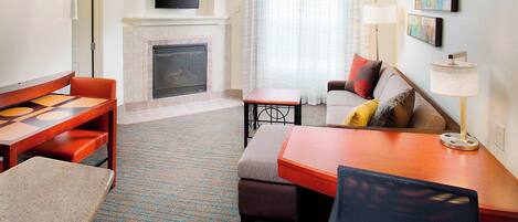 A hotel room with a fireplace, a TV mounted above it, a sofa, a table, and a chair.