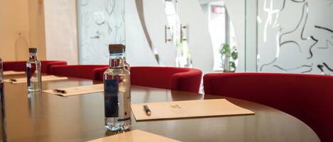 A conference table with water bottles, name cards, and red upholstered chairs in a modern interior with abstract wall art.
