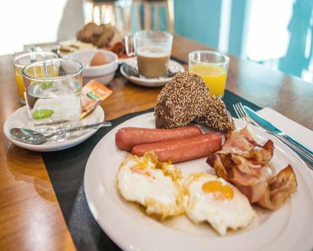 A breakfast plate with eggs, sausage, bacon, and a slice of bread on a hotel table.