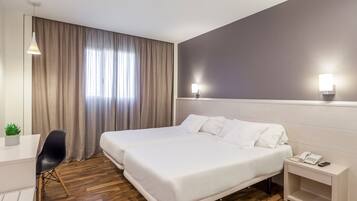 Habitación de hotel con dos camas, un escritorio, una silla, una planta pequeña y una mesita de noche con un teléfono.