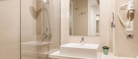 Een moderne badkamer met een douche met glazen wand, een witte wastafel, een spiegel en een haardroger aan de muur.
