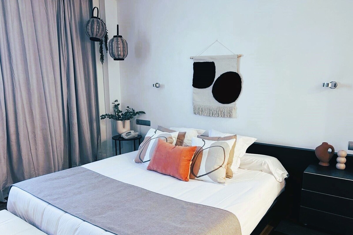 A modern bedroom with a large bed, a bedside table, a wall-mounted lamp, and a decorative piece.