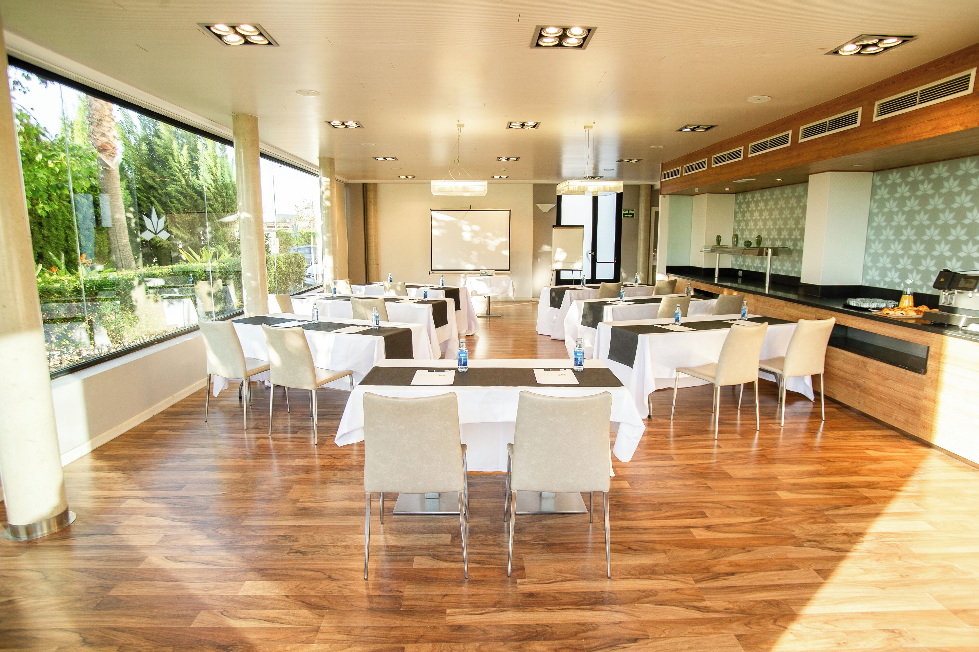A conference room with a long table, white chairs, and a projector screen.