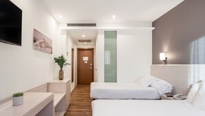 Quarto de hotel moderno com cama, mesa de cabeceira, luminária e televisão fixada na parede.