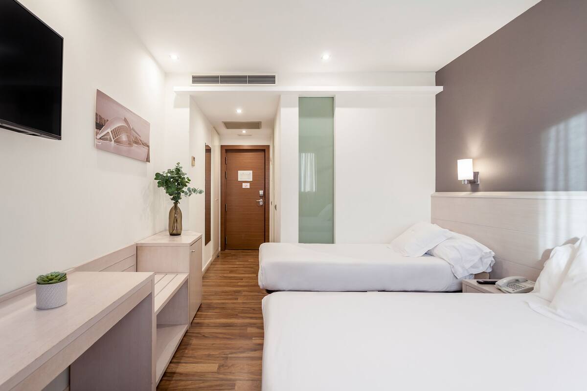 A modern hotel room with a bed, bedside table, lamp, and a TV mounted on the wall.