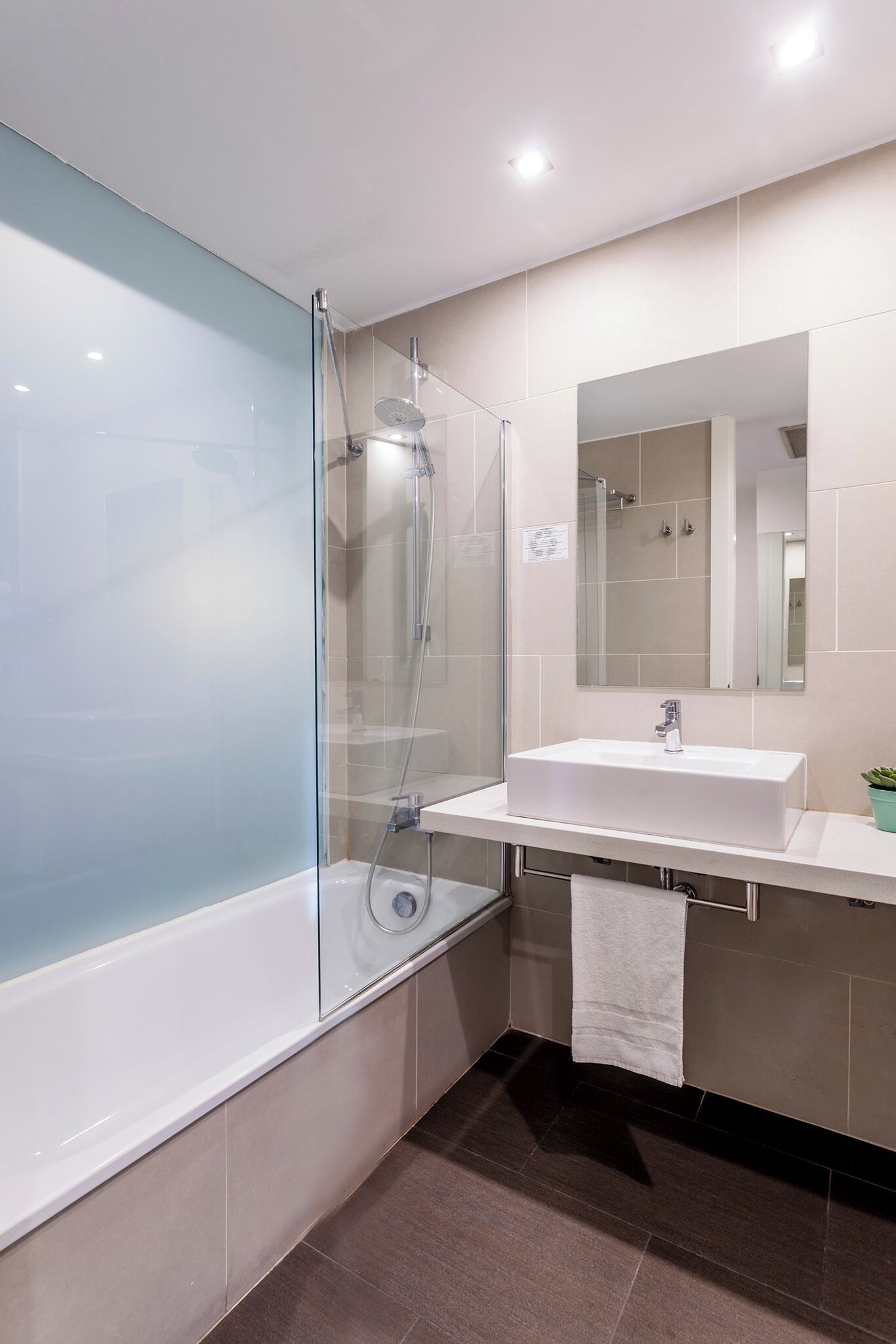 Un baño moderno con cabina de ducha de vidrio, un lavabo blanco y un espejo grande.