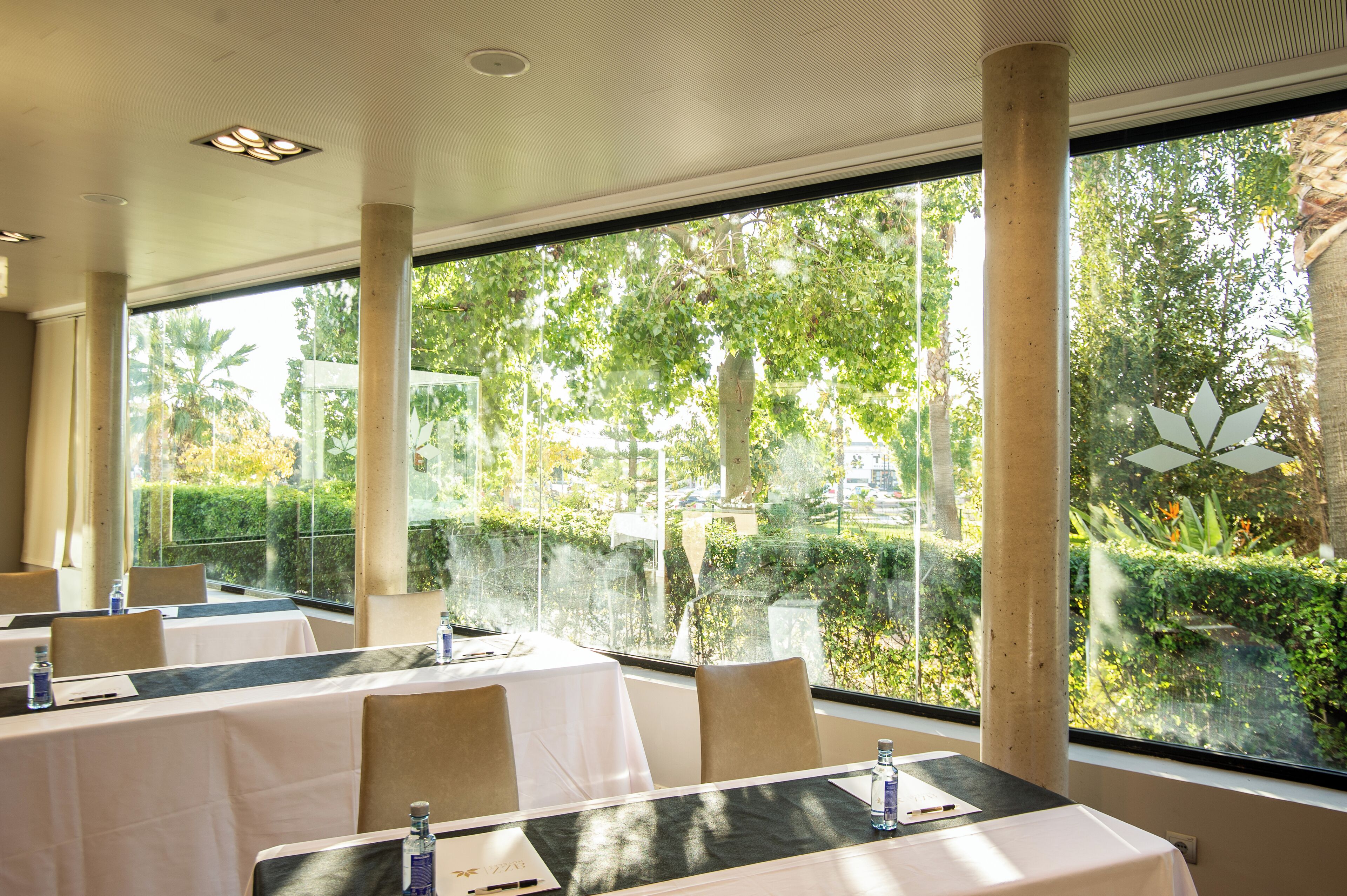 A restaurant with tables set for dining, large windows with a view of greenery and trees, and a modern interior design.